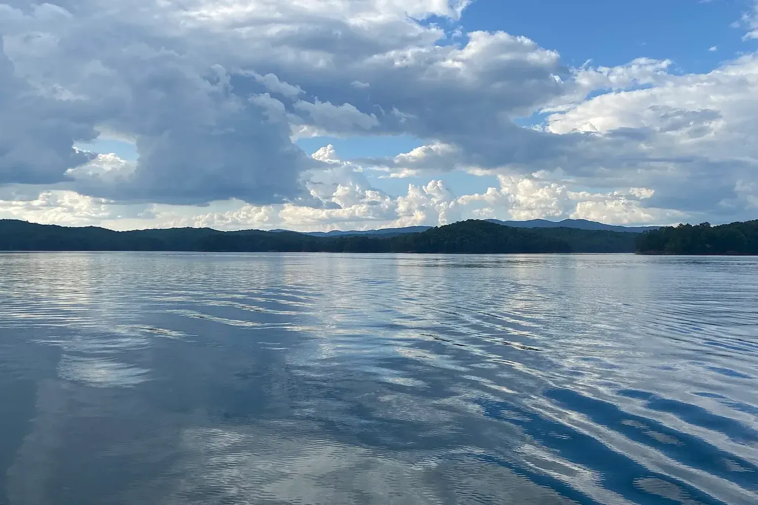 Still water on Carters Lake under a cloud-filled sky, with forested ridges along the far shore