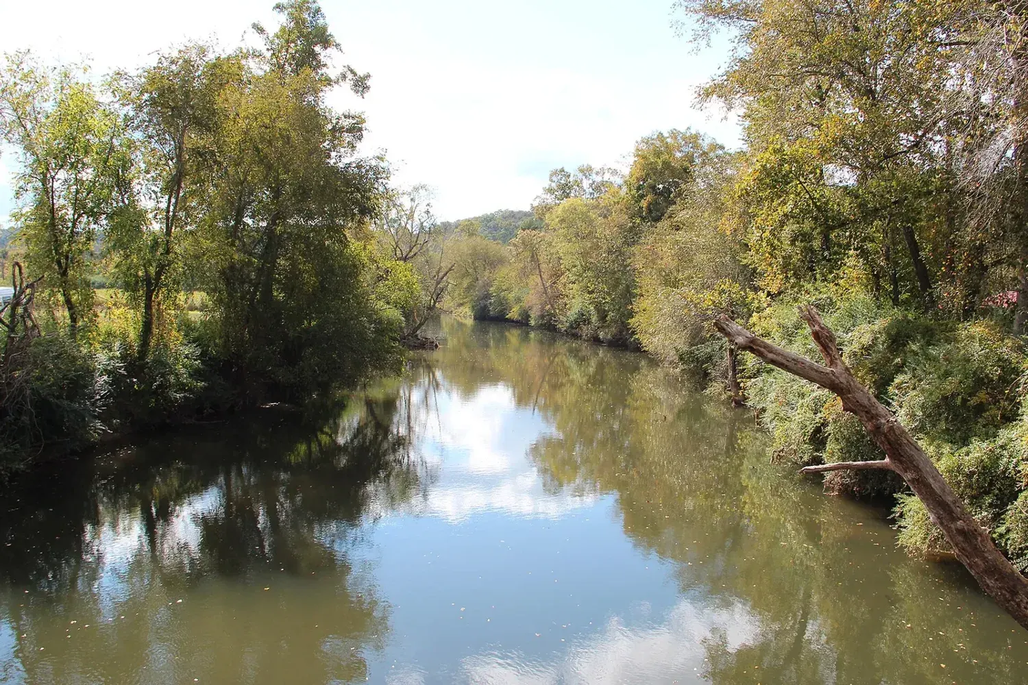 The Coosawattee River running still and wide between wooded banks turning autumn colours at Ellijay, Georgia